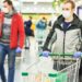Mann mit Mund-Nasen-Bedeckung und Handschuhen mit Einkaufswagen im Supermarkt