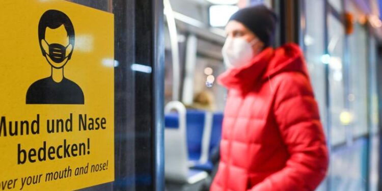 Ein Mann mit Schutzmaske steigt in eine Bahn ein.