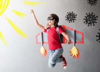 Kind mit Flugzeugflügeln und umkreist von Coronaviren springt einer gezeichneten Sonnen entgegen.