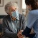 Seniorin mit medizinischer Maske wird zuhause von Ärztin betreut