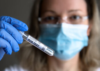 Frau mit medizinischer Maske hält einen COVID-19-Test in der Hand