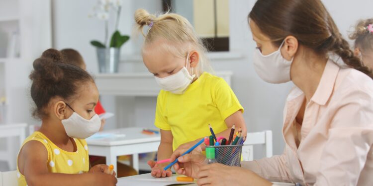 Erzieherin und zwei Kinder mit Mund-Nasen-Bedeckung