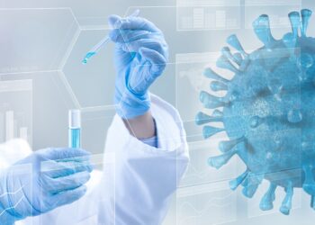 Forscherin mit Reagenzglas und einem groß eingeblendeten Coronavirus.