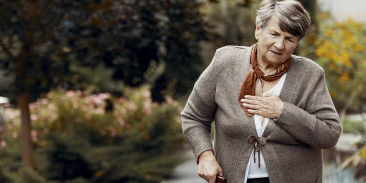 Donna anziana che tiene un bastone da passeggio che si abbraccia il petto a causa della mancanza di respiro