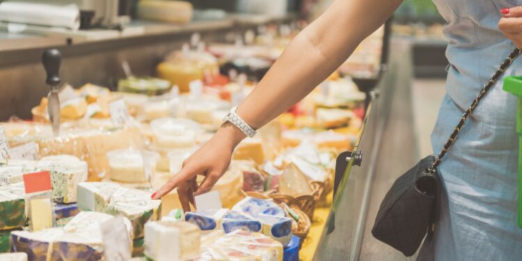 Eine Frau steht vor einer Käsetheke und zeigt auf einen Käse in der Auslage.