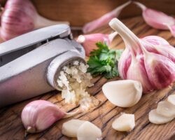 Frischer Knoblauch und Knoblauchpresse auf einem Holzbrett