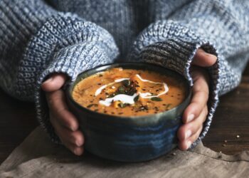 Weibliche Hände umfassen eine Schüssel mit Kürbissuppe