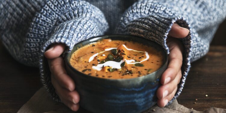 Weibliche Hände umfassen eine Schüssel mit Kürbissuppe