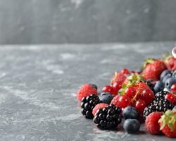 Verschiedene frische Beeren in einer Schüssel und auf einem Tisch