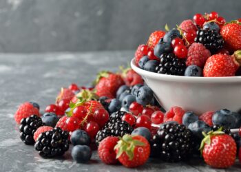 Verschiedene frische Beeren in einer Schüssel und auf einem Tisch