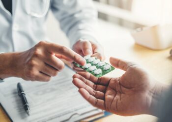 Ein Arzt reicht eine Packung Tabletten an einen Patienten.