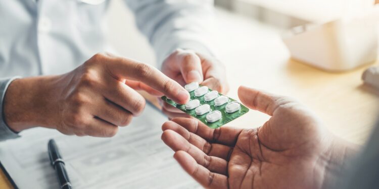 Ein Arzt reicht eine Packung Tabletten an einen Patienten.