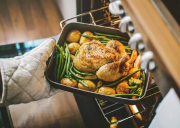 Eine Backform mit Hühnchen, Kartoffeln und Bohnen wird aus dem Ofen geholt