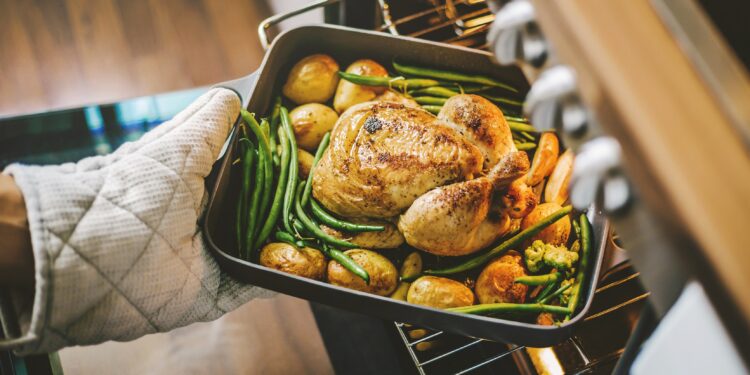 Eine Backform mit Hühnchen, Kartoffeln und Bohnen wird aus dem Ofen geholt