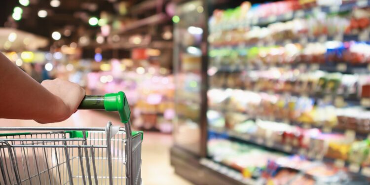 Eine Person schiebt einen Einkaufswagen durch einen Supermarkt.