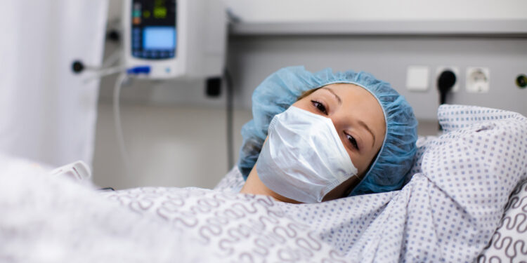 Patientin mit Mund-Nasen-Bedeckung im Bett im Krankenhaus