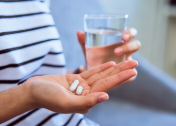 Frau mit zwei Tabletten in der einen und einem Glas Wasser in der anderen Hand