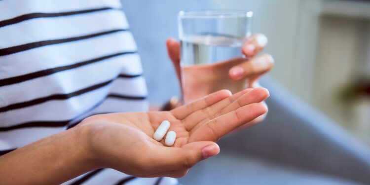 Frau mit zwei Tabletten in der einen und einem Glas Wasser in der anderen Hand