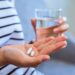 Frau mit zwei Tabletten in der einen und einem Glas Wasser in der anderen Hand