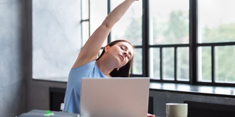 Zu hause am Laptop arbeitende Frau macht Dehnübungen