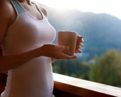 Eine Frau in Sportkleidung trinkt einen Kaffee auf einem Balkon.