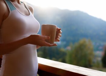 Eine Frau in Sportkleidung trinkt einen Kaffee auf einem Balkon.