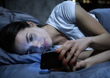 Eine Frau liegt im Bett und schaut auf ihr Smartphone.