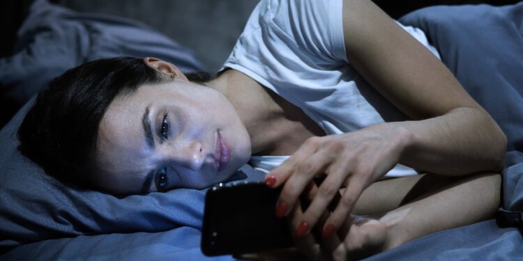 Eine Frau liegt im Bett und schaut auf ihr Smartphone.