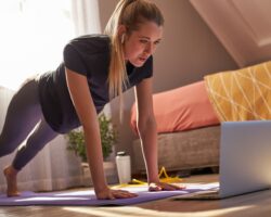 Junge Frau beim Online-Fitness-Kurs sieht auf ihren Laptop