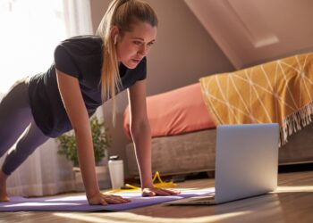 Junge Frau beim Online-Fitness-Kurs sieht auf ihren Laptop