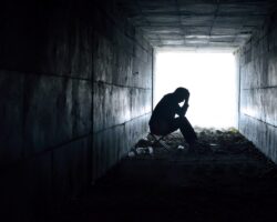 Eine Person sitzt am Ende eines dunklen Tunnels vor einem hellen Licht.