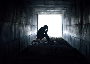 Eine Person sitzt am Ende eines dunklen Tunnels vor einem hellen Licht.