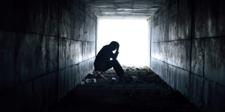 Eine Person sitzt am Ende eines dunklen Tunnels vor einem hellen Licht.