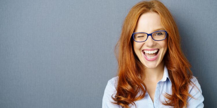 Rothaarige Frau mit Brille zwinkert mit einem Auge