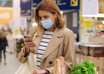 Eine Frau steht im Supermarkt und schaut auf ihr Handy.