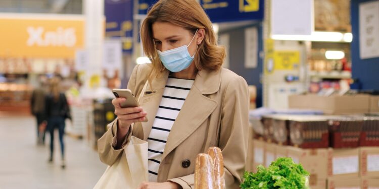 Eine Frau steht im Supermarkt und schaut auf ihr Handy.