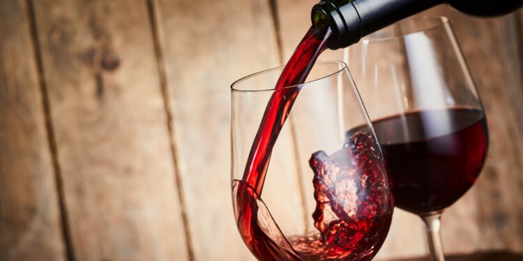 Aus einer Flasche wird Rotwein in ein Weinglas gegossen