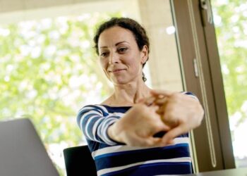 Eine Frau sitzt am Computer und streckt die Finger.