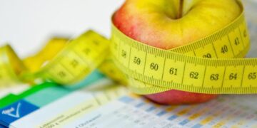 Ein Apfel und ein Maßband liegen neben einem Ernährungsplan.