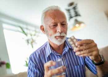 Mann hält seine blutdrucksenkenden Medikamente in der Hand und betrachtet sie.