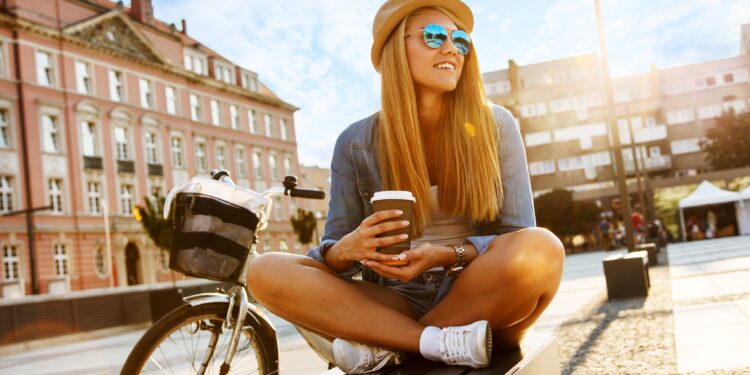 Junge Frau sitzt mit einem Einwegbecher vor ihrem Fahrrad