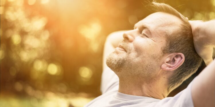 Mann entspannt mit geschlossen Augen in der Sonne.