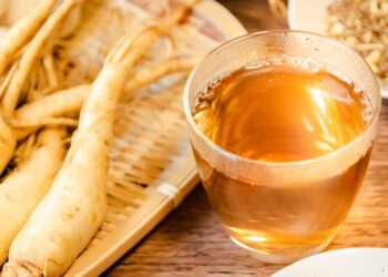 Ginseng-Wurzeln liegen neben einer Glastasse mit Ginsengtee