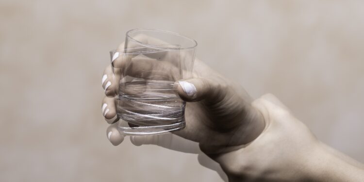 Eine zitternde Hand hält ein Glas mit Wasser fest.