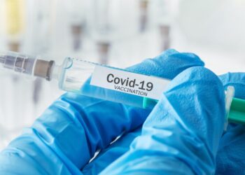 Behandschuhte Hand hält eine Spitze mit der Aufschrift Covid-19