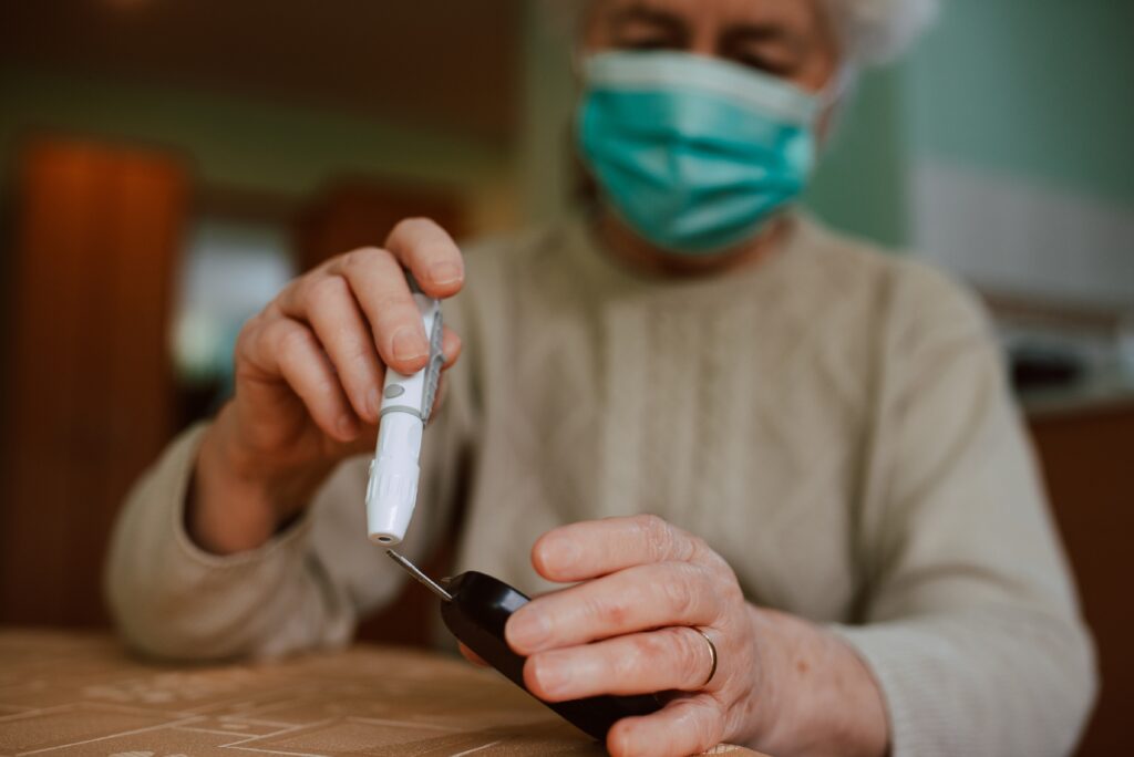 Seniorin mit Gesichtsmaske hält ein Blutzuckermessgerät in der Hand