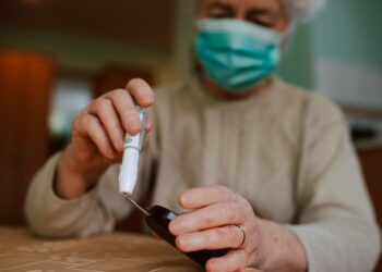 Seniorin mit Gesichtsmaske hält ein Blutzuckermessgerät in der Hand