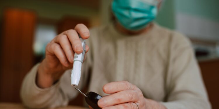 Donna anziana che indossa una maschera facciale con in mano un misuratore di glicemia