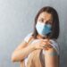 Frau mit medizinischer Maske zeigt ihr Pflaster auf dem Oberarm
