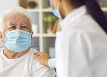 Ärztin und älterer Patient mit Mund-Nasen-Schutz